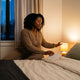 Woman closing a book and reaching for the bedside lamp in a warm, dim bedroom — building a consistent bedtime routine
